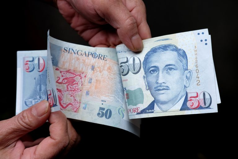 Closeup shot of a person holding Singapore dollars in front of a black background