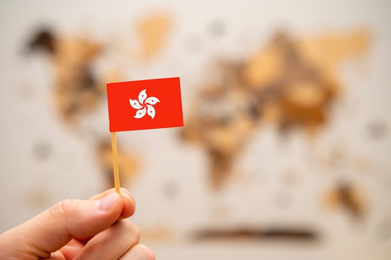 Hong Kong flag in mans hand on the world map background.