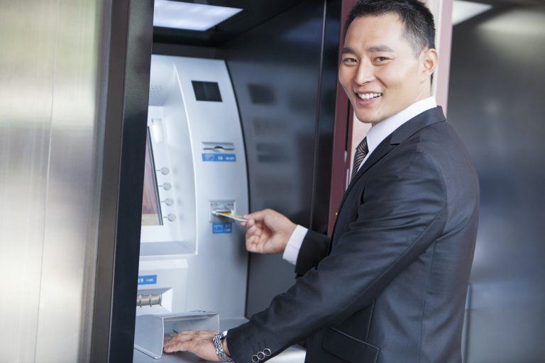 Smiling businessman using ATM with bank card